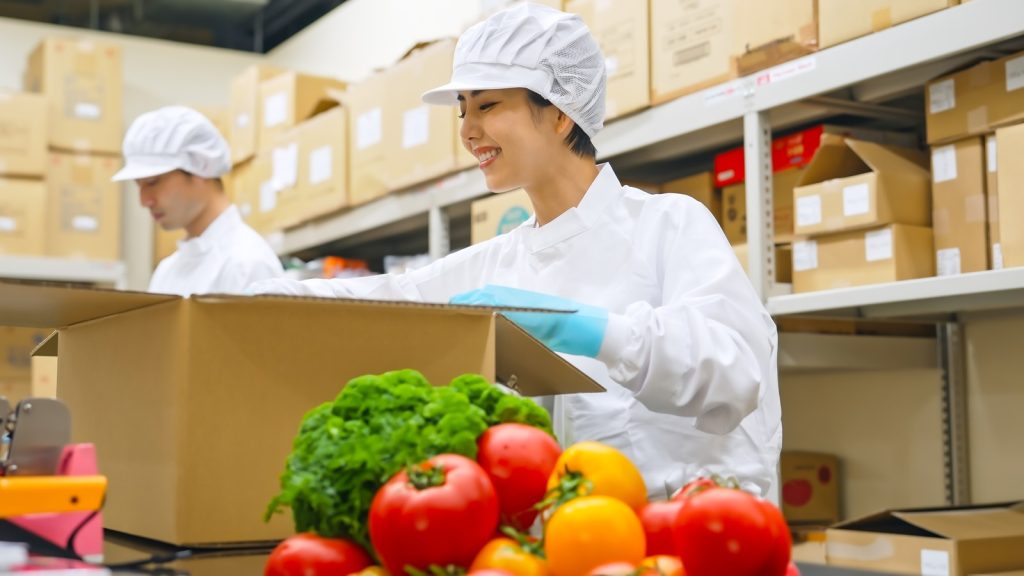 Workers in proper hygienic clothing sort vegetables for shipping from a cold storage facility